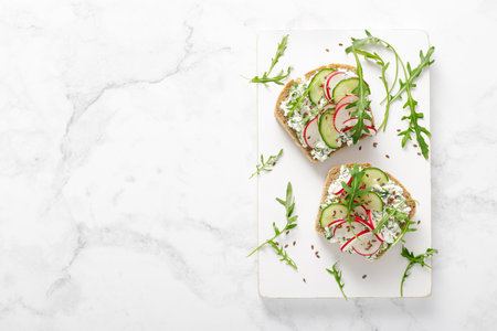 Sandwiches with rye bread toasts, cottage cheese, radish, cucumber, fresh greens and arugula for a healthy breakfast, top viewの写真素材