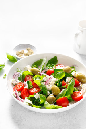 Fresh healthy vegetable Mediterranean salad of feta cheese, tomato, olives, green pepper and green basil leavesの写真素材