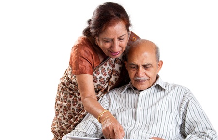 A senior Indian / Asian couple pointing at a newspaper - isolated on whiteの写真素材