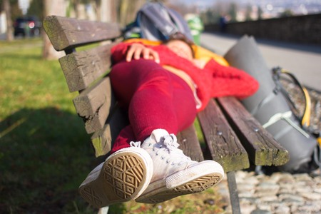 Girl sleeping on wood bench outdoors. Outside female lyingの写真素材
