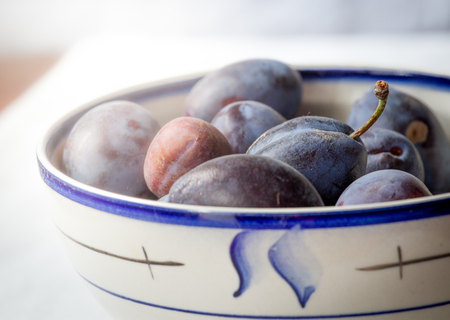 Blue plums in plate on white table. Fruit isolated.