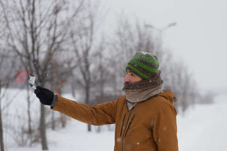 Man shoot by the small camera in deeply snow. Cold nature, storm in the urban park. Outdoor activity.の写真素材