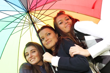 happy smiling girlfriends stay under colourful umbrella  の写真素材