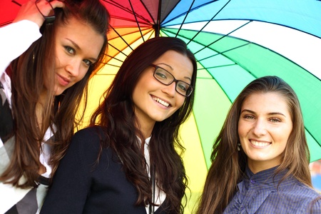 happy smiling girlfriends stay under colourful umbrella  の写真素材
