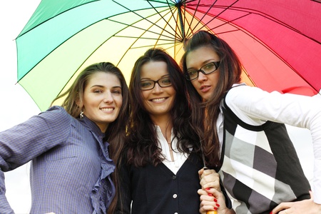 happy smiling girlfriends stay under colourful umbrella  の写真素材