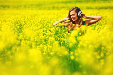  Young woman with headphones listening to music on oilseed flowering fieldの写真素材