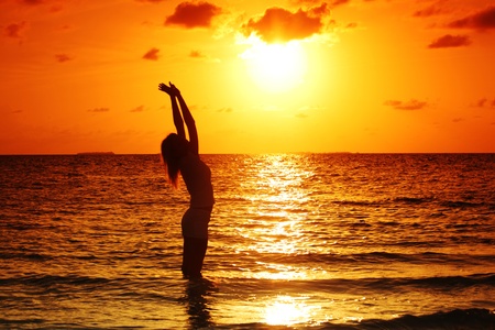 happy woman standing on a sunset in ocean wavesの写真素材