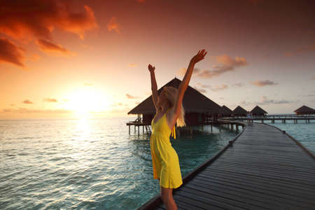 woman in a dress on a bridge home sea and the maldivian sunset on the backgroundの写真素材