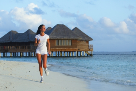 Beautiful young woman in white sportswear running on beachの写真素材