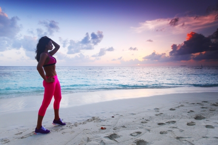 Beautiful fit woman standing on beach under sunset lightの写真素材