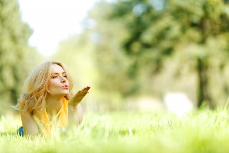 Happy young woman lying on grass and blowing kissの写真素材