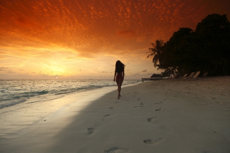 Young woman walking on beach under sunset lightの写真素材