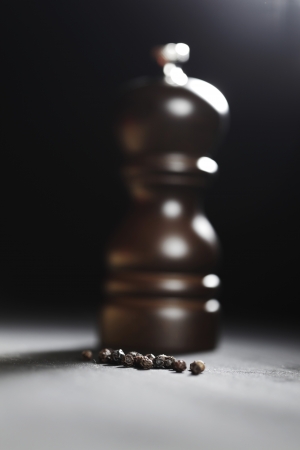 Wooden peppermill with peppercorns on black tableの写真素材