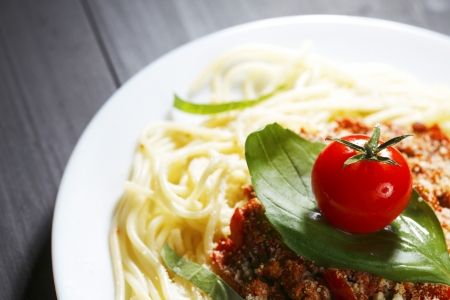 Spaghetti bolognese with fresh basil and tomato in white plate on back tableの写真素材