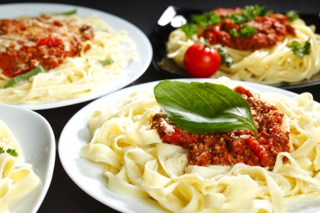 Spaghetti bolognese with basil in white plates on black tableの写真素材