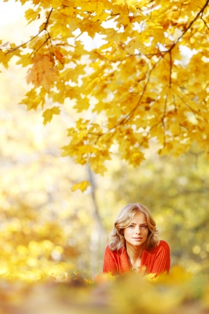 Happy young woman laying on autumn leaves in parkの写真素材