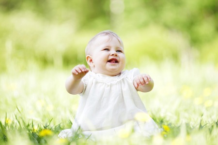 Adorable baby girl sitting on grass in park at sunny dayの写真素材