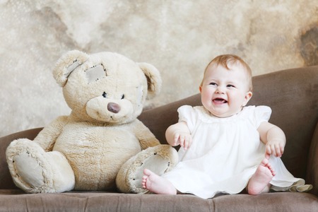 Smiling baby girl in dress sitting with teddy bearの写真素材