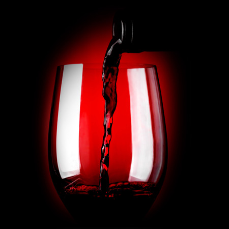 Red wine pouring in glass on dark backgroundの写真素材