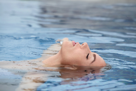 Young woman enjoying water and sun in outdoor swimming poolの写真素材