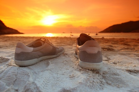 Shoes on beach on sunset with orange sky over seaの写真素材
