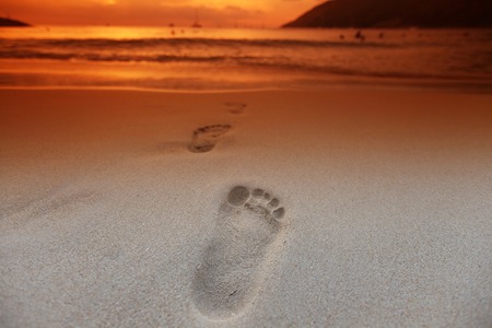 Footprints on the beach at sunset with orange skyの写真素材