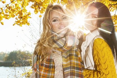 Two cheerful women in autumn park at sunny dayの写真素材