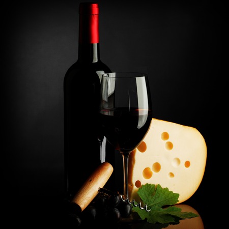 Red wine bottle, glass, cheese and corkscrew on dark backgroundの写真素材