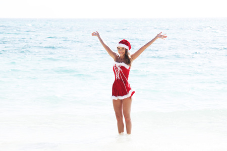 Beautiful woman in Mrs. Claus custume on tropical beach, Christmas vacations conceptの写真素材
