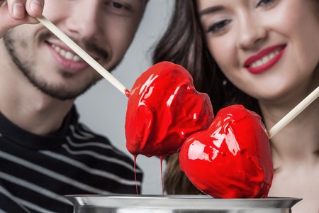 Fondue of love, loving couple dips chocolate hearts in red glazeの写真素材