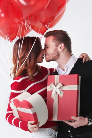 Happy kissing couple in love holding Valentines day gifts and bunch of heart shaped balloonsの写真素材