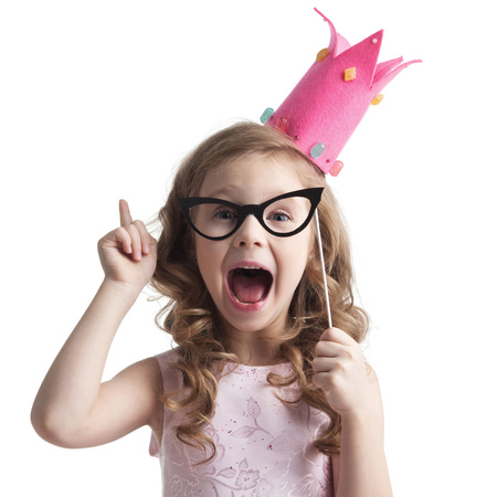Funny princess girl in pink dress and crown holding party glasses on stick and saying something smart with finger upの写真素材