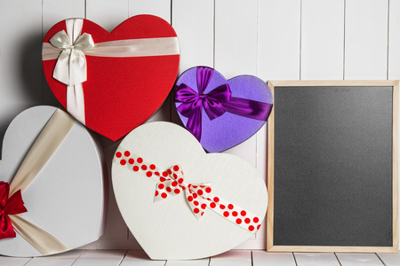 Heart shaped Valentines Day gift boxes and blackboard on white wooden background