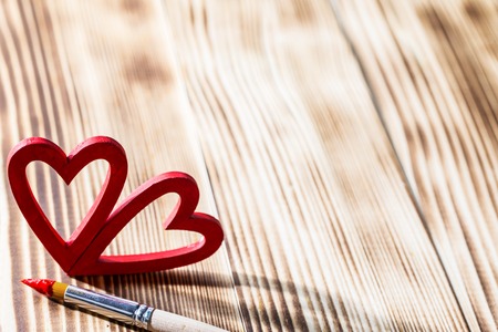 Two wooden red painted Valentine day hearts and paint brush on wooden backgroundの写真素材