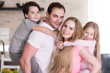 Portrait of happy family, father and mother giving boy and girl piggy back ride at home