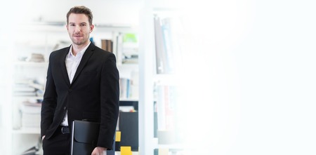 Businessman holding a briefcase in office, white copy space