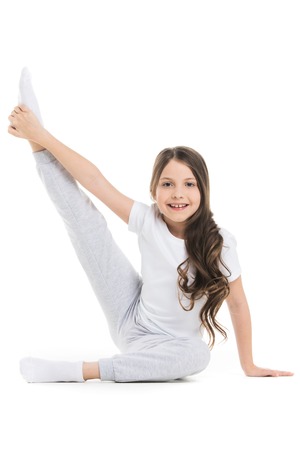 Small girl doing stretching leg exercise isolated on white backgroundの写真素材