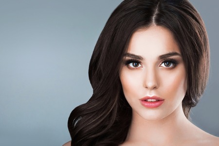 Beautiful woman with long wavy brown hair. Closeup beauty portrait of a fashion model posing at studio on gray backgroundの写真素材