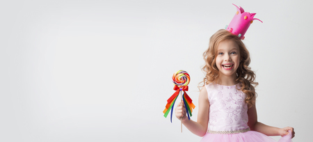 Small princess girl in crown holds a large spiral decorated lollipop candyの写真素材