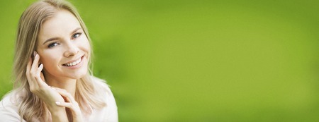 Closeup of young beautiful smiling blond woman, on green background of summer natureの写真素材