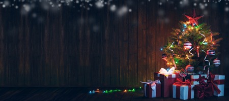 Decorated Christmas tree with glowing lights and gift boxes on wooden backgroundの写真素材