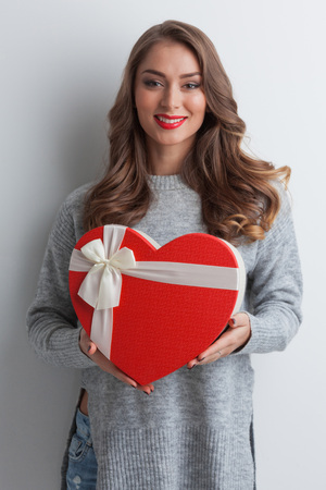 Young girl with red heart-shaped gift box on white backgroundの写真素材