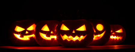 Many Halloween Pumpkin glowing faces in a row on dark backgroundの写真素材