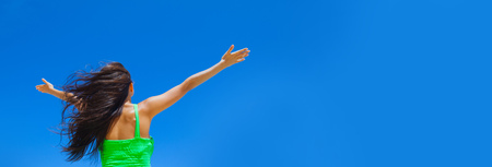 Young woman with raised hands over blue sky backgroundの写真素材