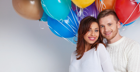 Young smiling couple with colorful balloons on whiteの写真素材