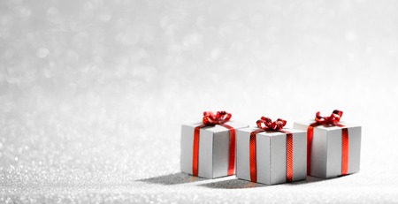 Small decorative Christmas gift boxes with red ribon bows on silver glitter background with copy...