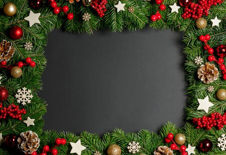 Christmas Border frame of tree branches on black background with copy space , red and wooden decor, berries, stars, conesの写真素材