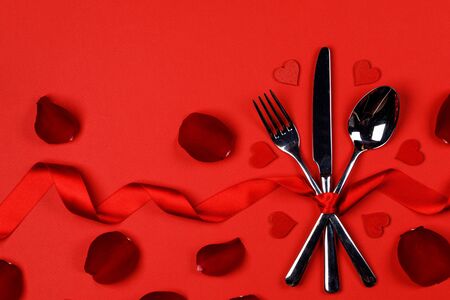 Cutlery set tied with silk ribbon rose flower petals and hearts on red background Valentine day dinner conceptの写真素材