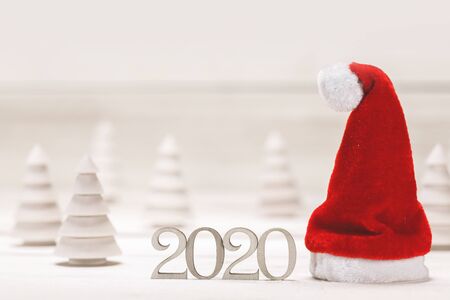 Conceptual 2020 new year background with small wooden fir trees 2020 number and red santa claus hatの写真素材