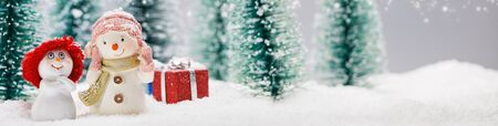Two small cute snowmen friends with gifts in forest under falling snowの写真素材